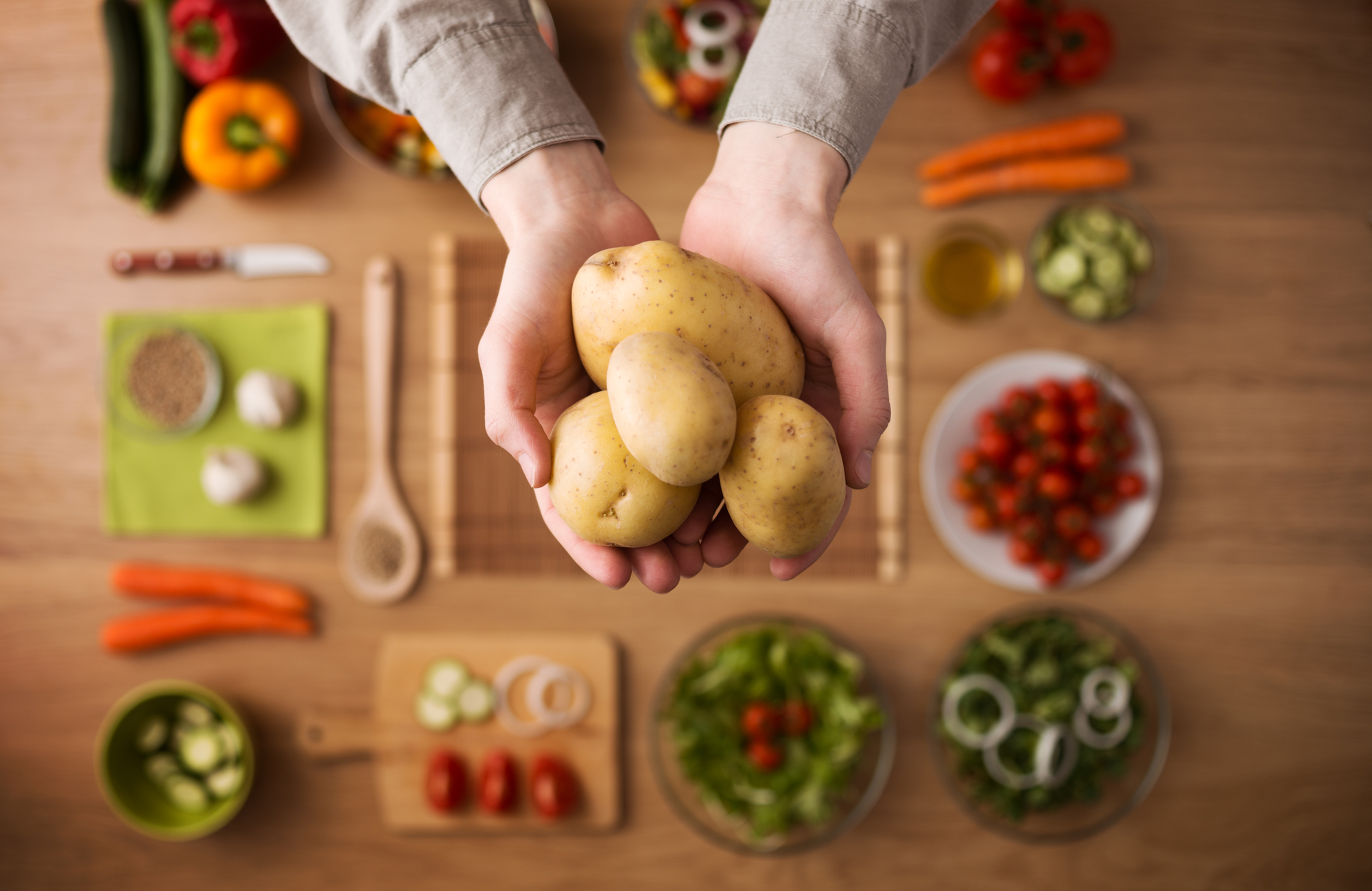 Hands holding fresh harvested potatoes with raw colorful seasonal vegetables on background, top view